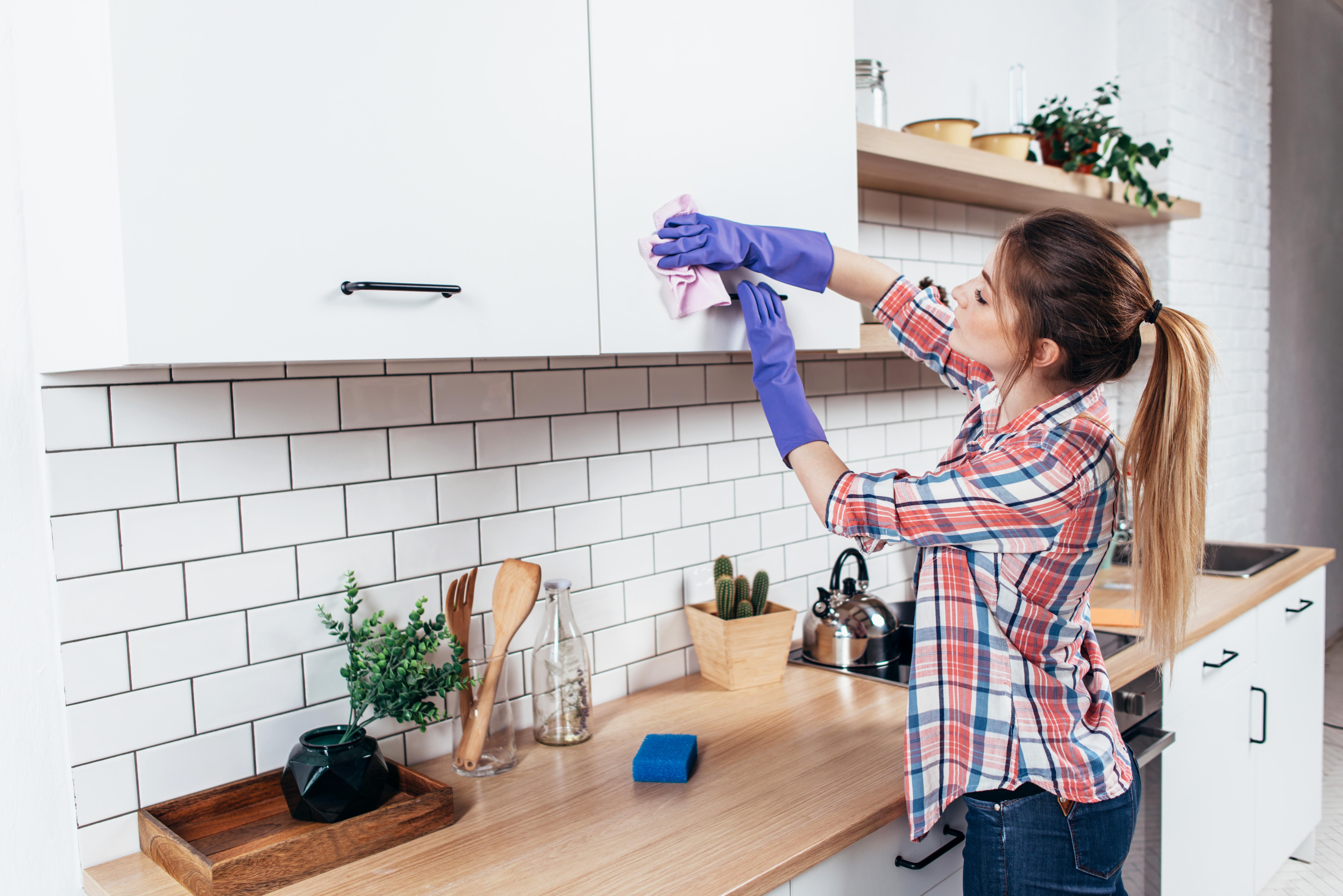 Frau putzt Küchenschrank mit einem feuchten Lappen.